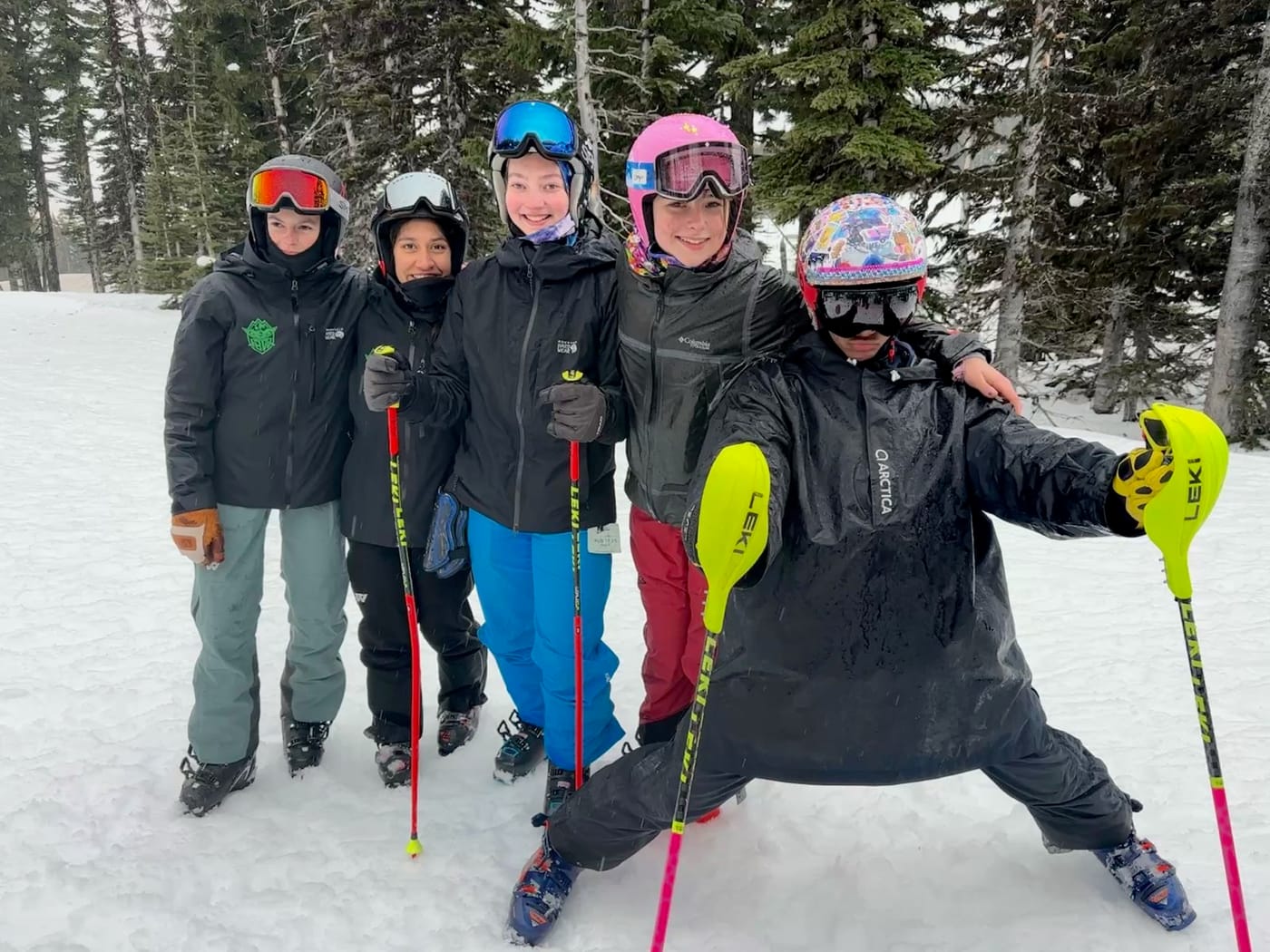Five racers on a wet day, one striking a pose in a rain poncho with slalom guards raised