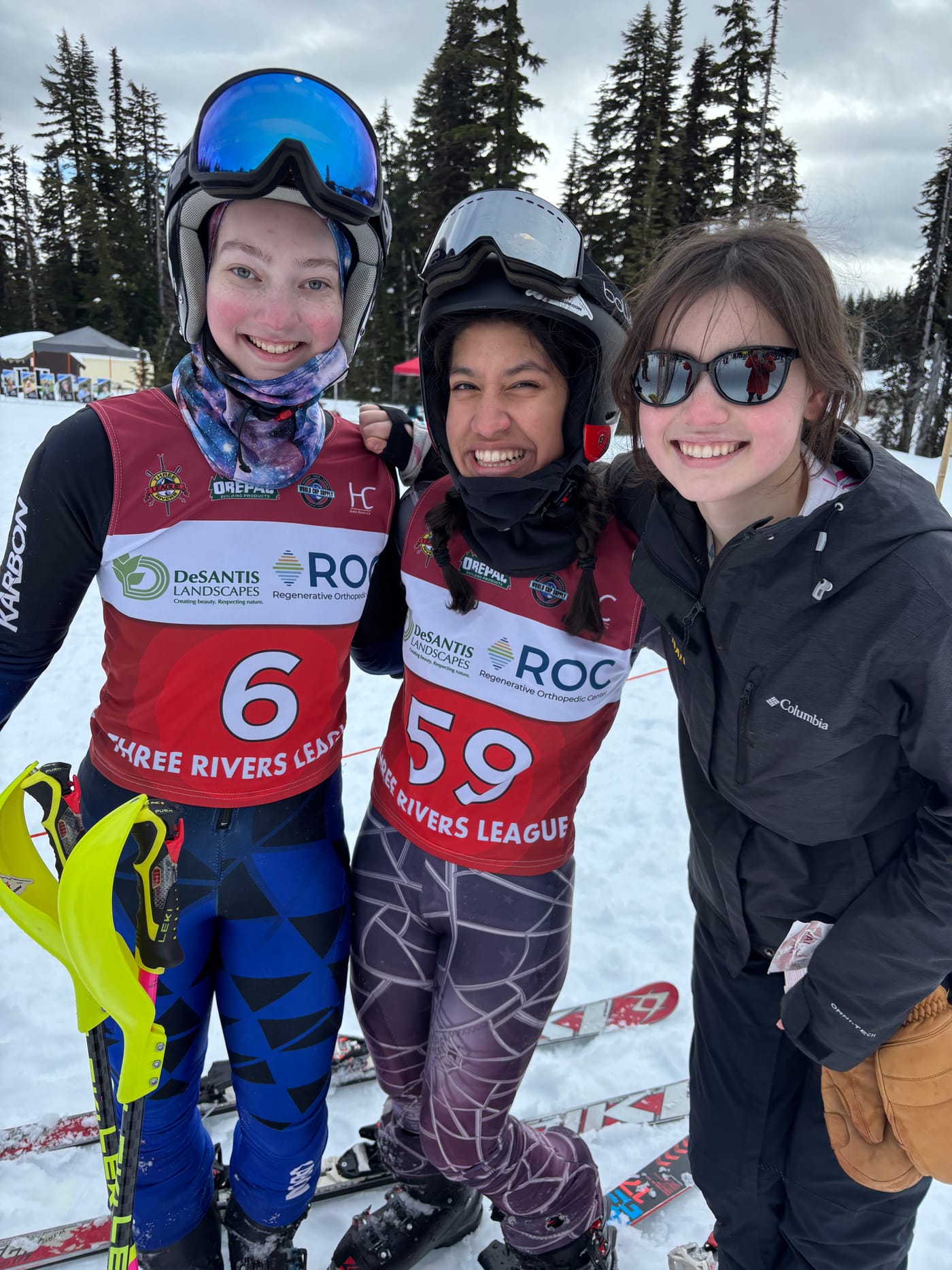 Three racers in Three Rivers League bibs crowded into frame, laughing, skis and poles stacked behind